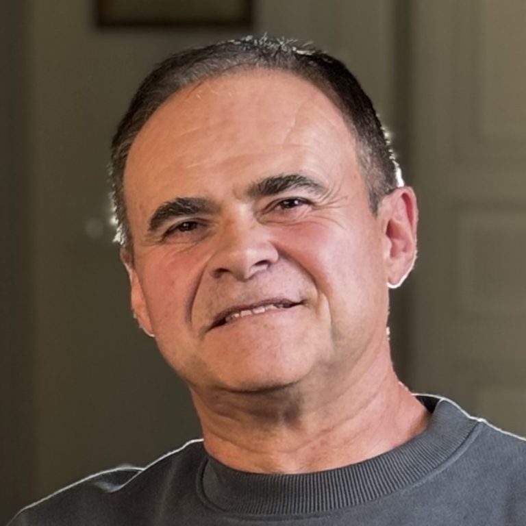 Portrait de Jean-Paul, webmaster WordPress. C'est un homme de 60 ans aux cheveux bruns et aux yeux marrons, habillé d’une chemise bleue.